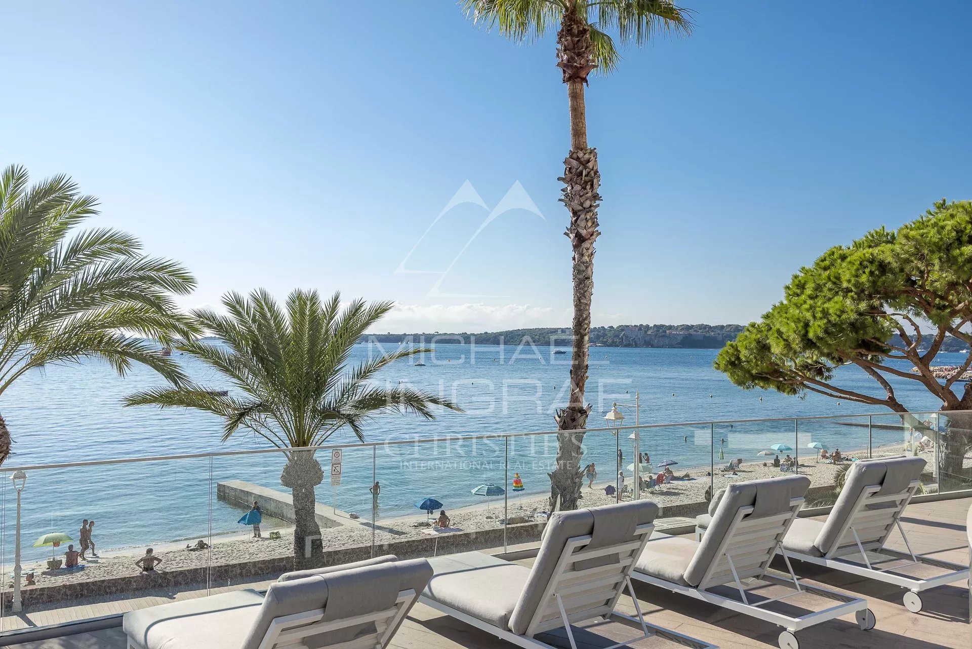 Vue sur la mer depuis une terrasse avec des transats et des palmiers à Cannes.