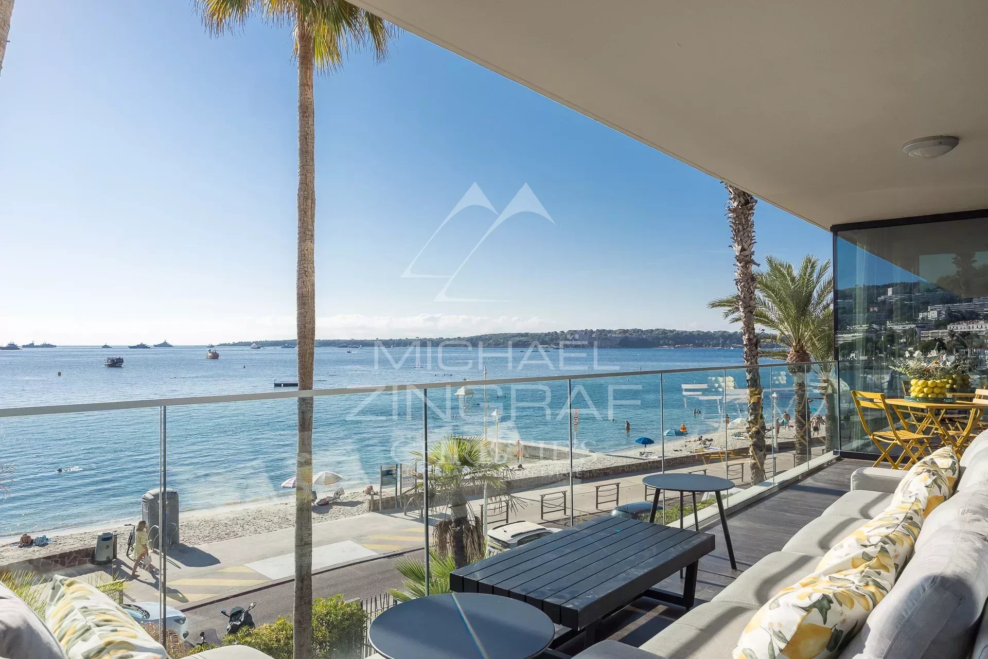 Vue panoramique sur la mer depuis une terrasse d'un triplex à Cannes, avec des palmiers et des bateaux au loin.