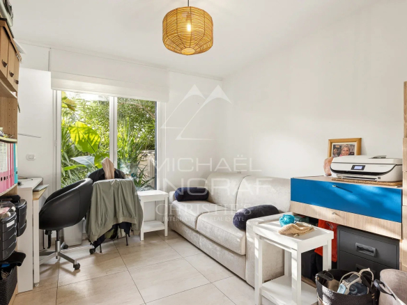 Intérieur d'un appartement avec un coin salon et une fenêtre donnant sur un jardin.
