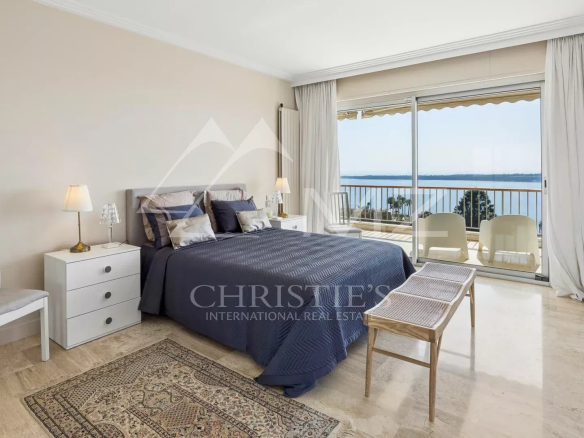 Bedroom with a queen bed, navy cover, and white nightstands facing a sea-view balcony.