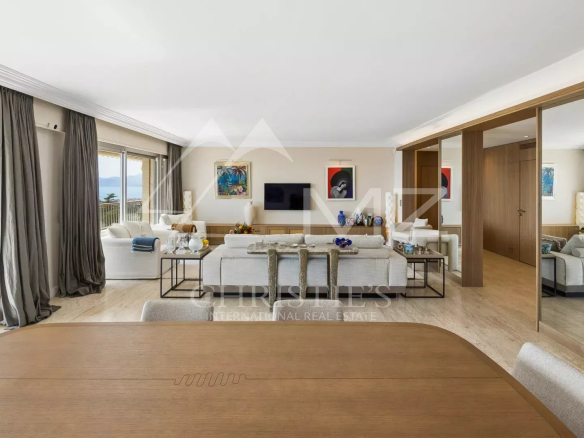 Spacious open-plan living area with sea-view balcony, white sofas, glass tables, and colorful artwork.