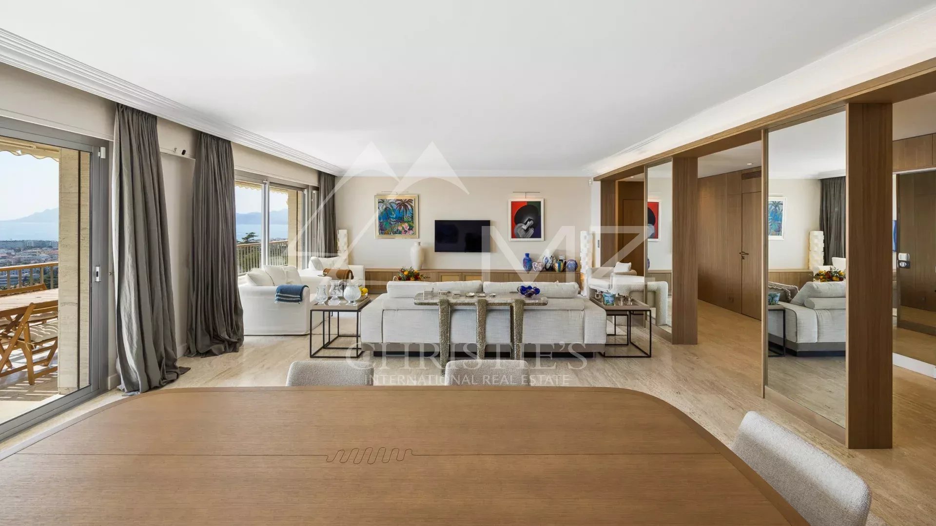 Spacious open-plan living area with sea-view balcony, white sofas, glass tables, and colorful artwork.