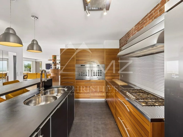 Modern kitchen with wood and stainless steel elements, open to a bright living space.