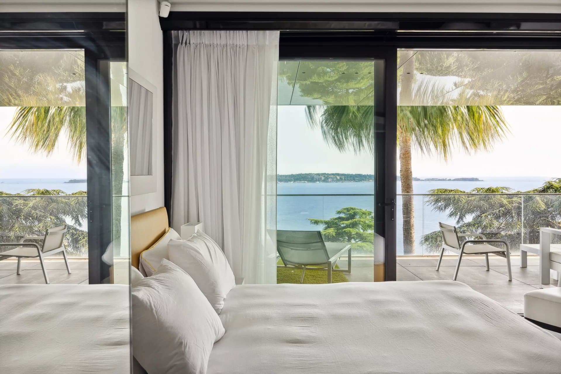 Chambre d'un appartement de luxe avec vue sur la mer à Cannes, terrasse et palmiers visibles.