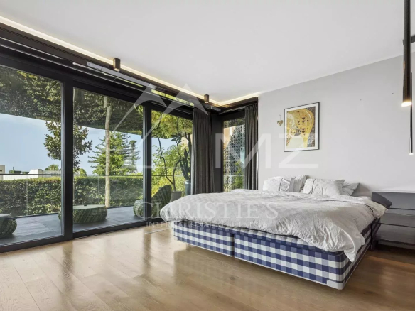 Bedroom in a contemporary apartment with a bed and large bay windows overlooking a garden.