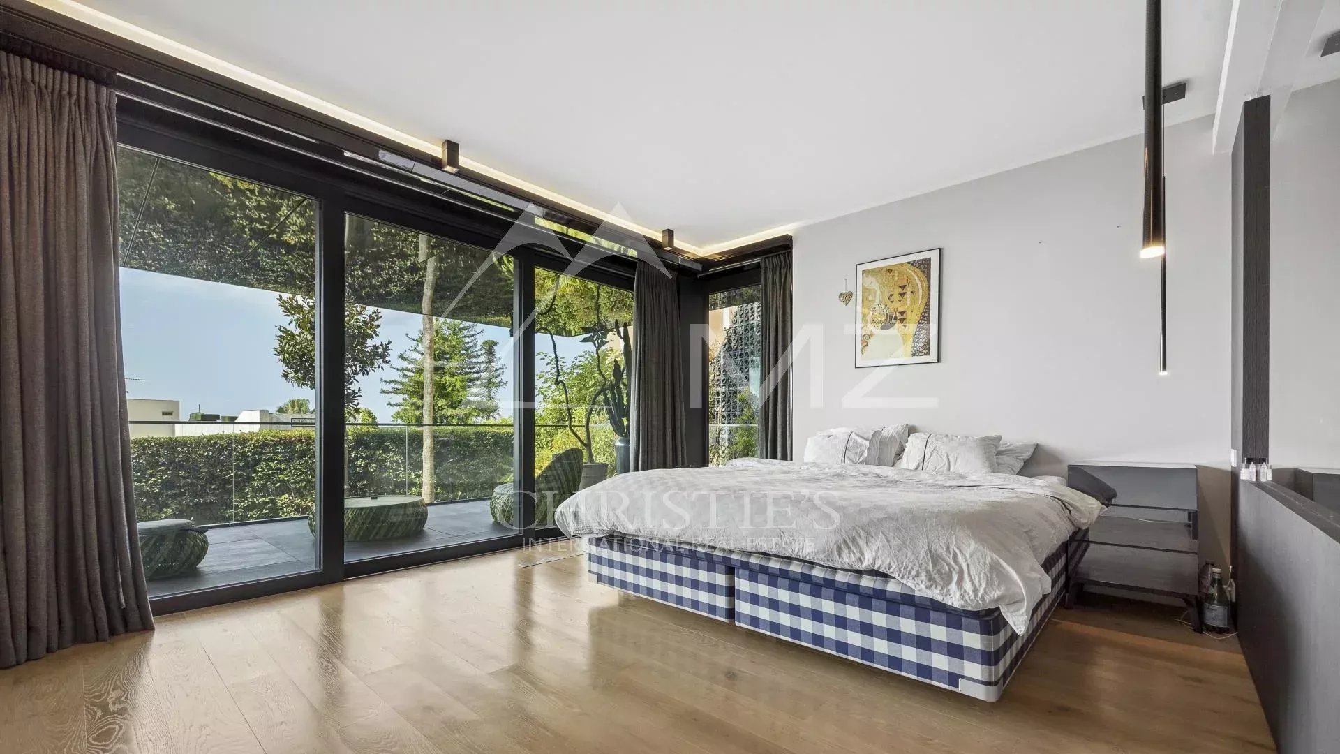 Bedroom in a contemporary apartment with a bed and large bay windows overlooking a garden.