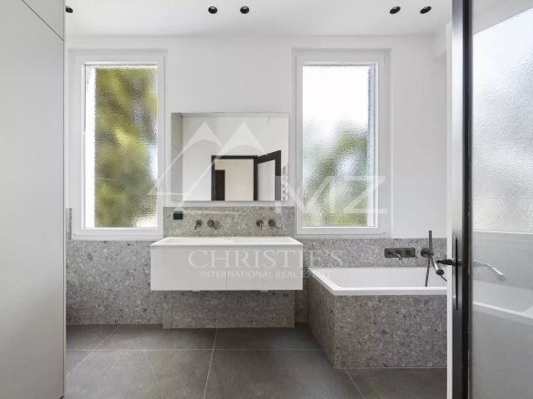 Salle de bains moderne avec baignoire et vasque en pierre, fenêtres avec vue sur la verdure.