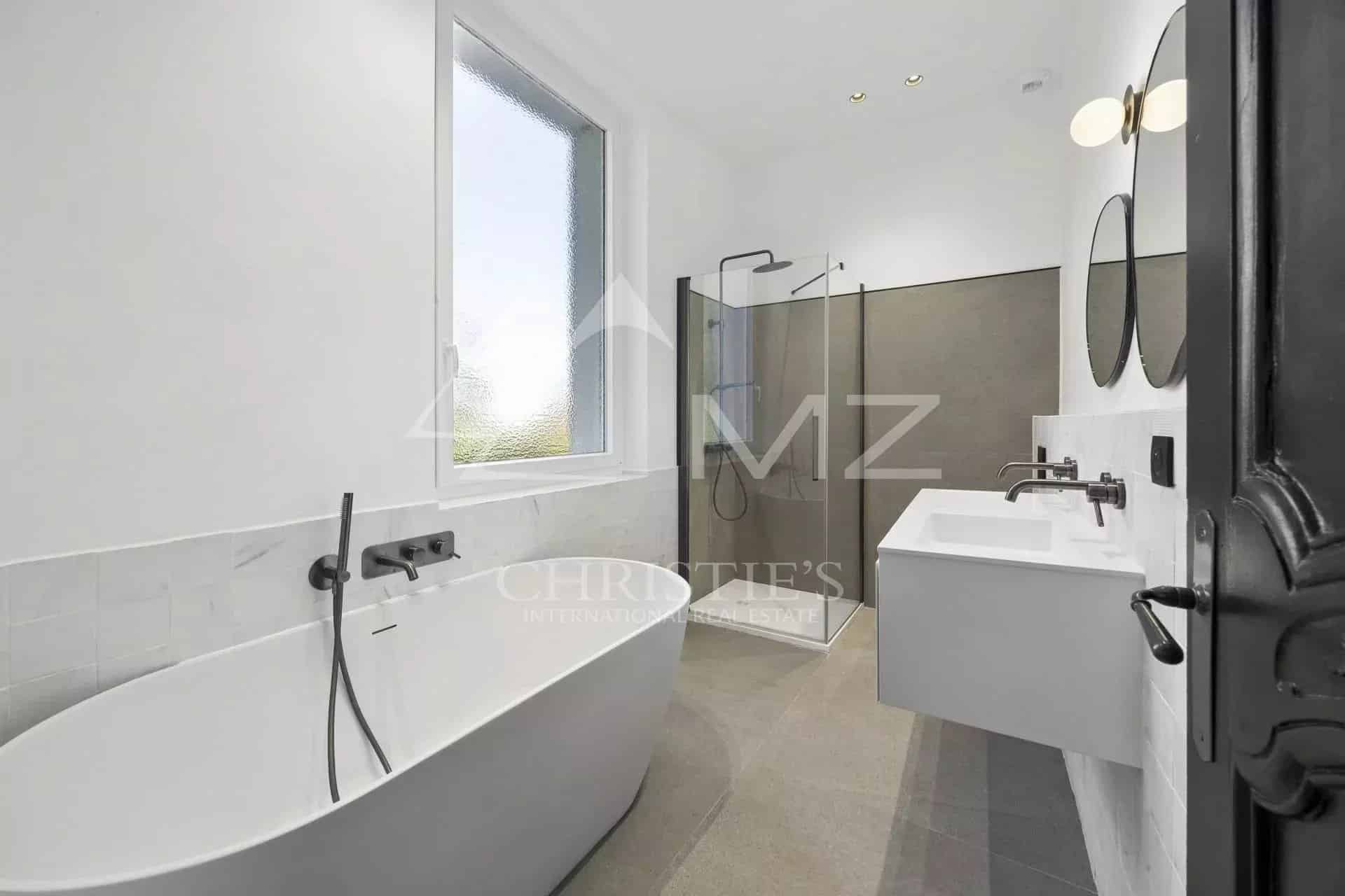 Salle de bain moderne avec baignoire, douche et double vasque dans un appartement rénové.
