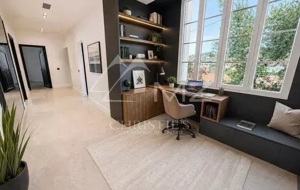Intérieur d'un appartement rénové avec un coin bureau et de grandes fenêtres laissant entrer la lumière.
