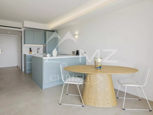 Intérieur d'un appartement rénové avec cuisine moderne et table ronde, vue sur mer à Cannes.