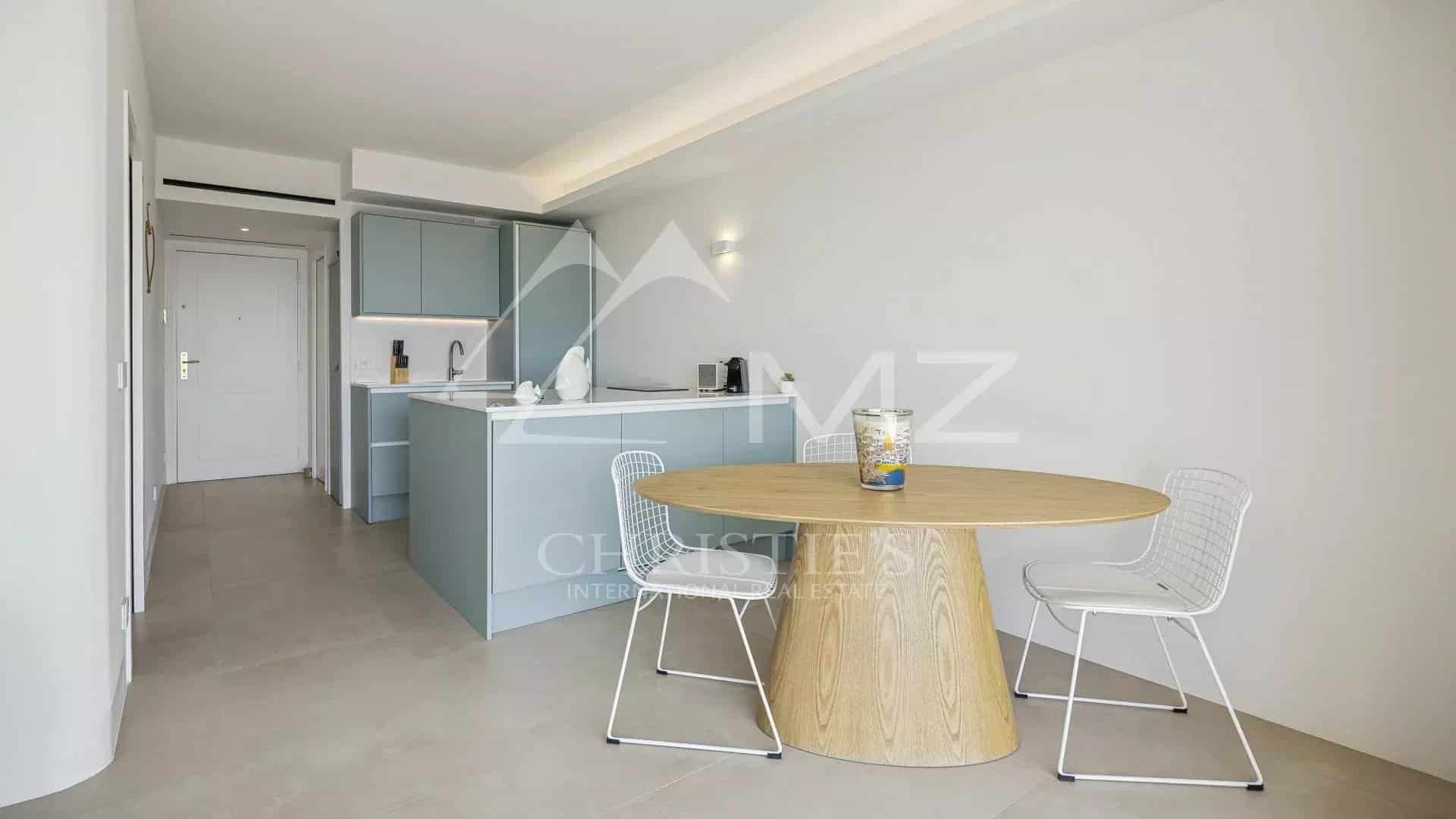 Intérieur d'un appartement rénové avec cuisine moderne et table ronde, vue sur mer à Cannes.