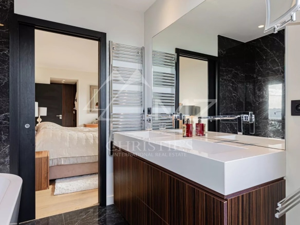 Modern bathroom with sink, mirror and bathtub, overlooking a bedroom.