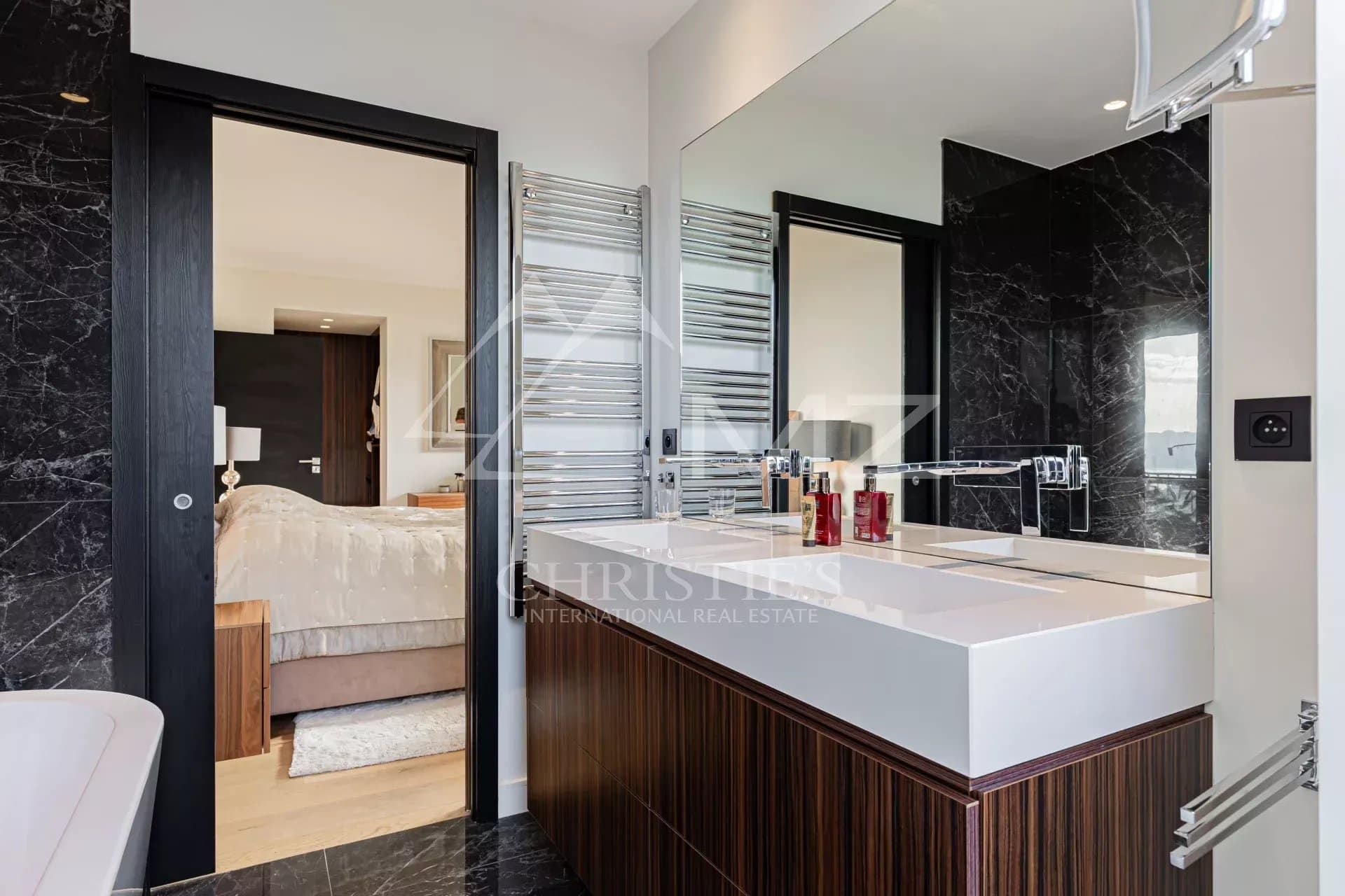 Modern bathroom with sink, mirror and bathtub, overlooking a bedroom.