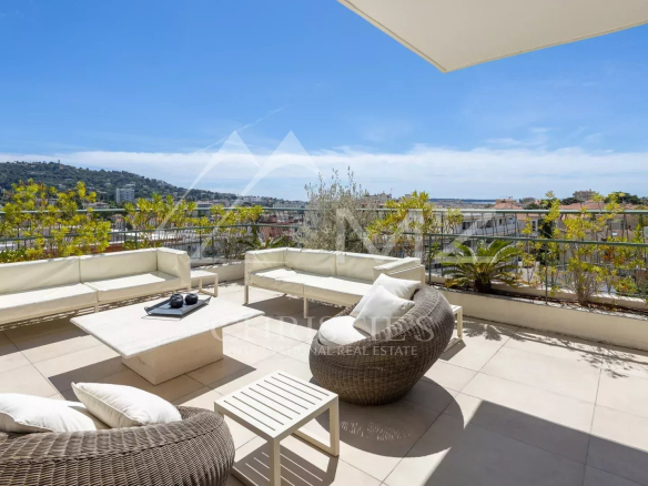 Terrace of a villa in Cannes with views of the hills and the sea, comfortable outdoor furniture.