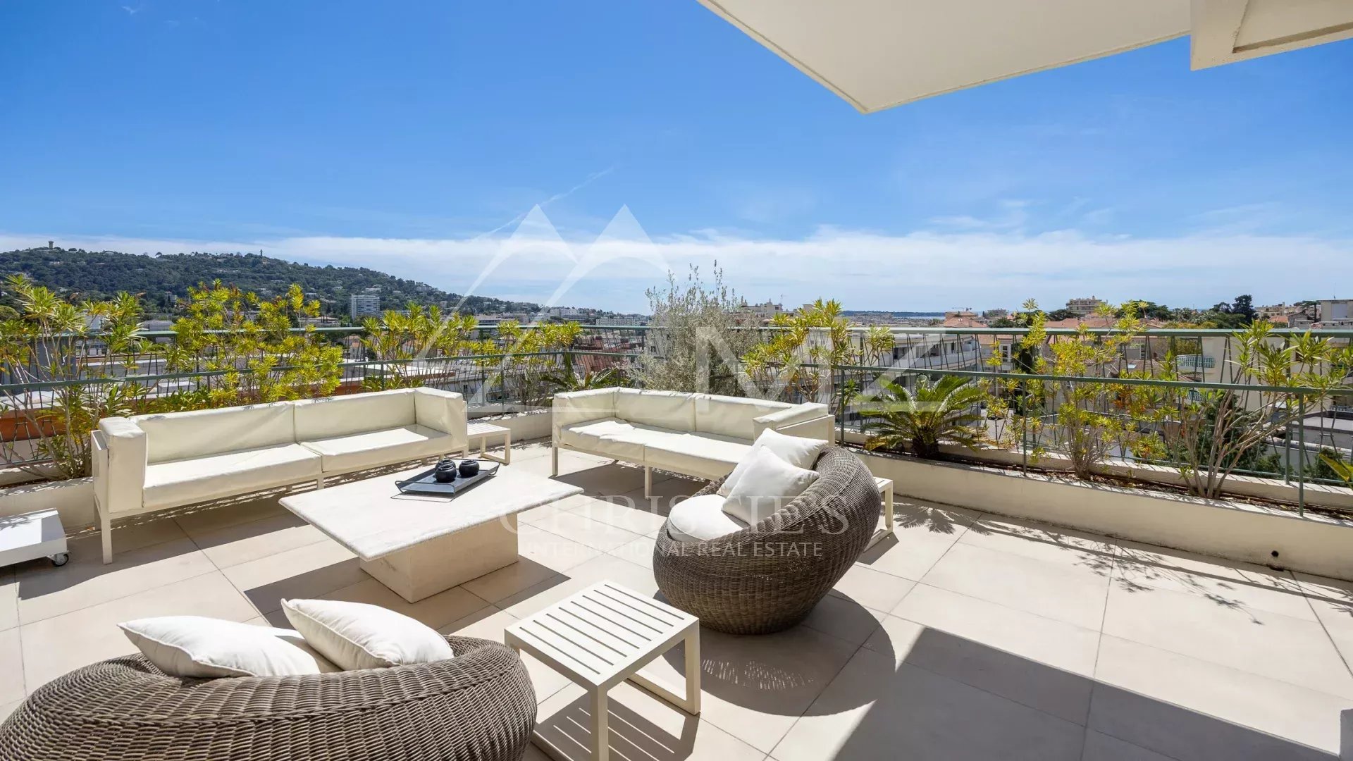 Terrace of a villa in Cannes with views of the hills and the sea, comfortable outdoor furniture.