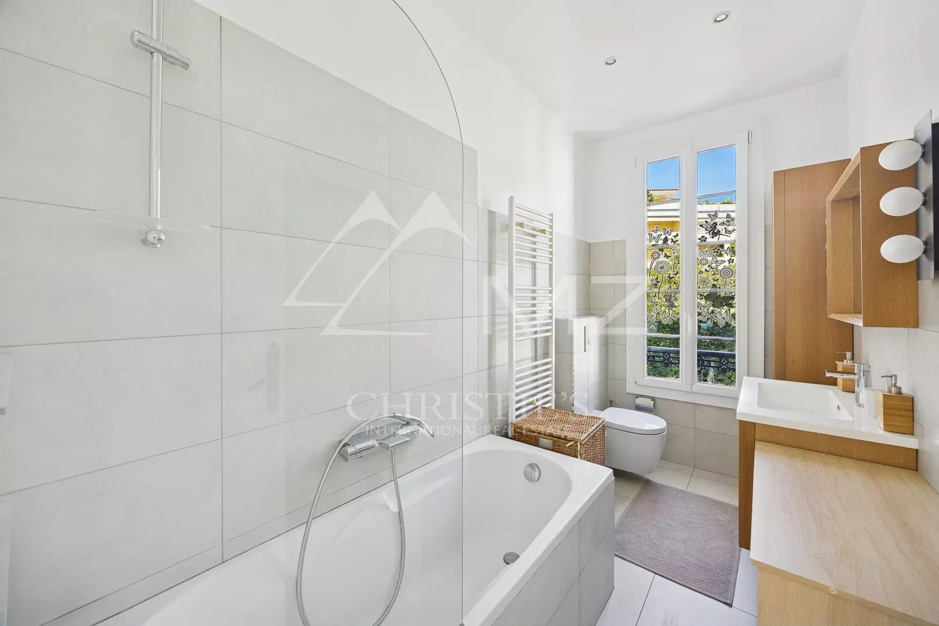 Salle de bains d’un appartement à Cannes Salle de bains lumineuse avec baignoire et fenêtre donnant sur l'extérieur.