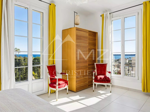 Intérieur d'un appartement au dernier étage avec vue sur la mer, deux chaises rouges et fenêtres lumineuses.