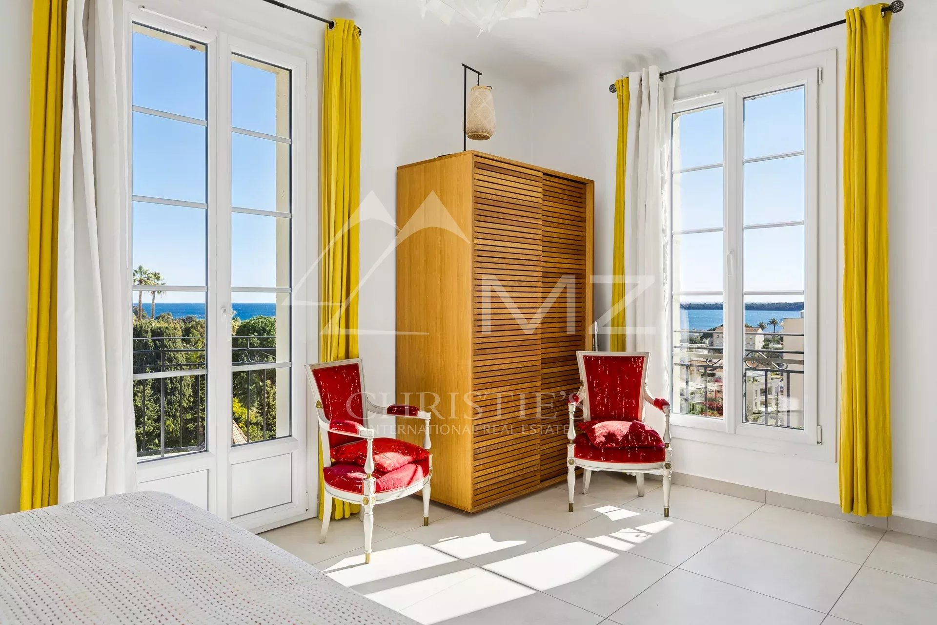 Appartement avec vue mer à Cannes Intérieur d'un appartement au dernier étage avec vue sur la mer, deux chaises rouges et fenêtres lumineuses.