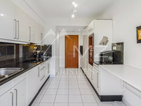 Cuisine moderne et spacieuse d'un appartement à Cannes, avec meubles blancs et plans de travail en noir.