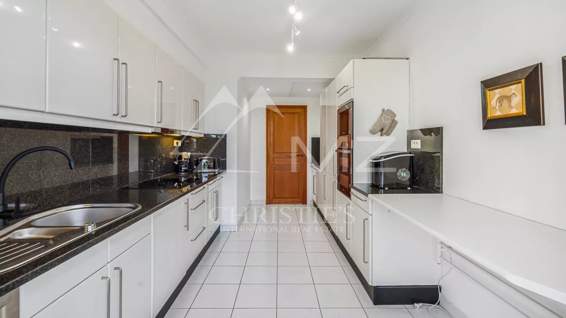 Cuisine moderne et spacieuse d'un appartement à Cannes, avec meubles blancs et plans de travail en noir.