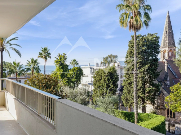 Vue depuis la terrasse d'un appartement à Cannes, avec des palmiers et l'église Saint-Georges en arrière-plan.