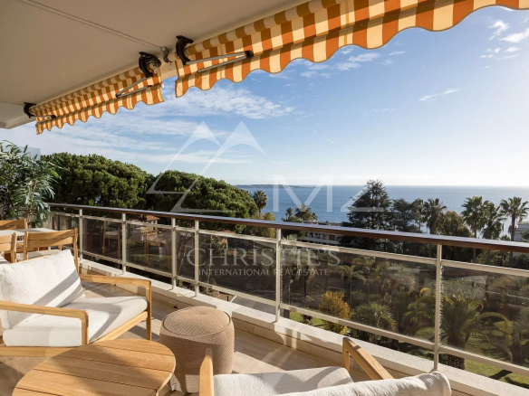 Terrasse d'un appartement à Cannes avec vue panoramique sur la mer et des sièges en bois.