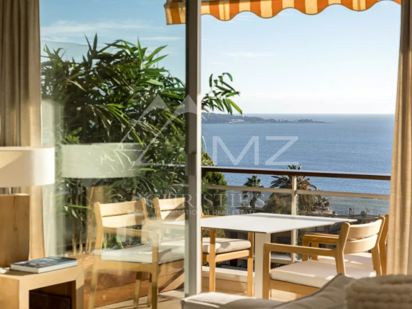 Intérieur d'un appartement avec vue sur la mer à Cannes, fenêtres ouvertes sur un balcon.