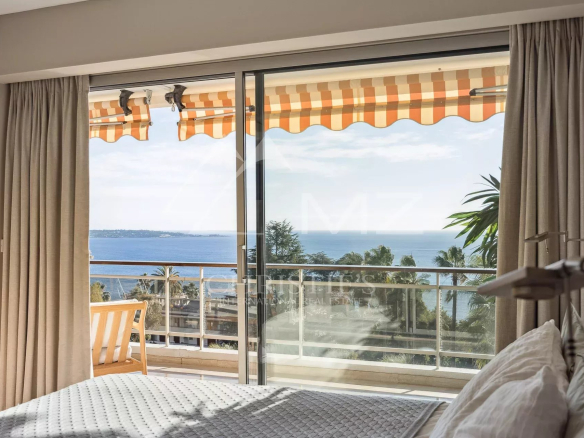 Vue panoramique sur la mer depuis un appartement à Cannes avec balustrade et rideaux.