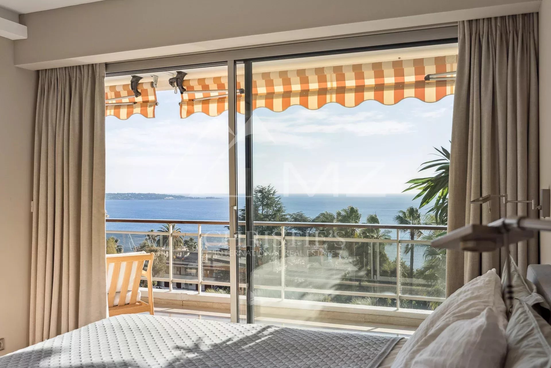 Appartement avec vue mer à Cannes Vue panoramique sur la mer depuis un appartement à Cannes avec balustrade et rideaux.