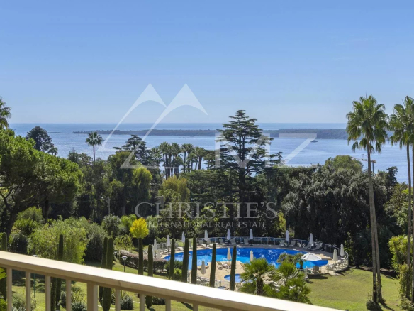 Vue panoramique depuis un appartement à Cannes, avec piscine et parc verdoyant en premier plan.