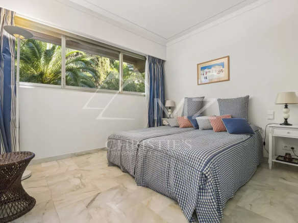 Chambre d'appartement à Cannes avec lit double et fenêtre donnant sur un jardin.