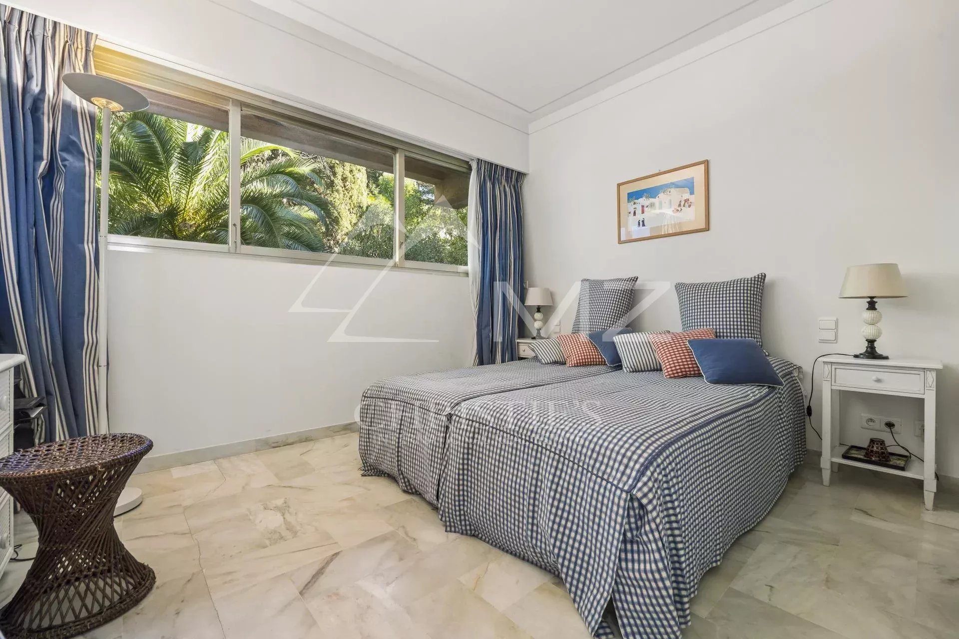 Chambre d'appartement à Cannes avec lit double et fenêtre donnant sur un jardin.
