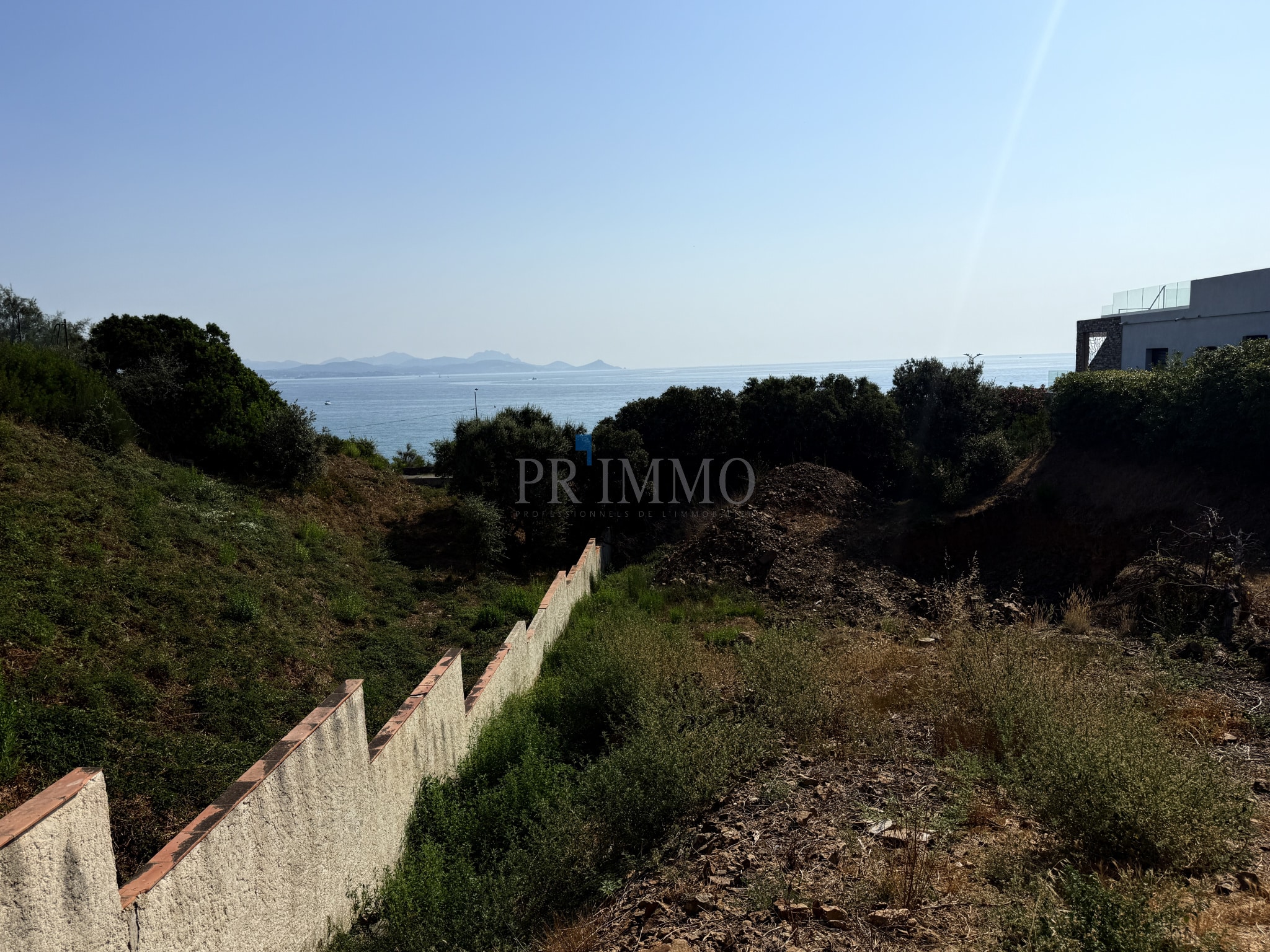 Terrain à bâtir avec vue sur la mer aux Issambres, entouré de végétation.
