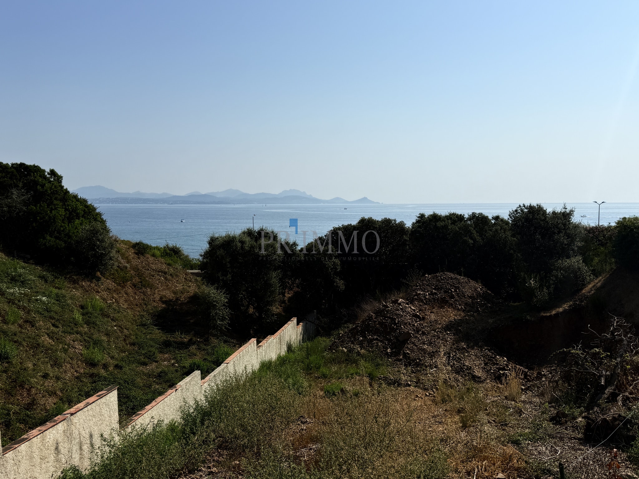Terrain à bâtir avec vue sur la mer aux Issambres, entouré de végétation.