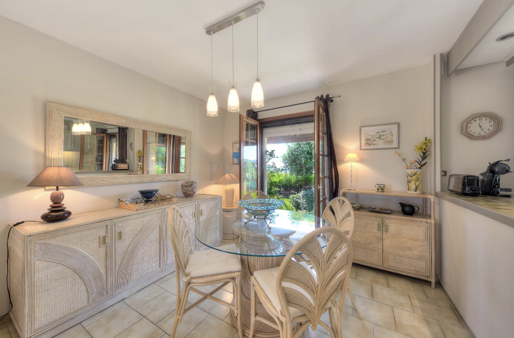 Bright dining room with glass table and wicker chairs, overlooking the garden.