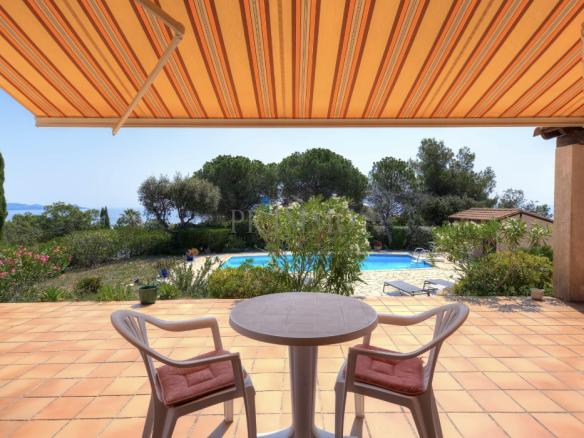 Terrace of a villa with sea view, table and chairs, swimming pool in the background.