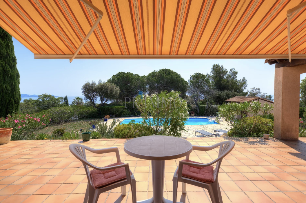 Terrace of a villa with sea view, table and chairs, swimming pool in the background.