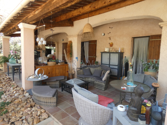 Terrasse d'une villa avec mobilier en rotin et décoration intérieure, entourée de verdure.