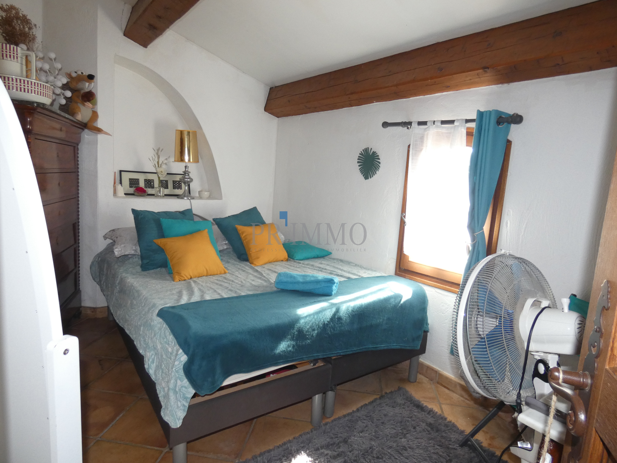 Chambre d'une villa avec lit double, oreillers colorés et ventilateur au plafond.