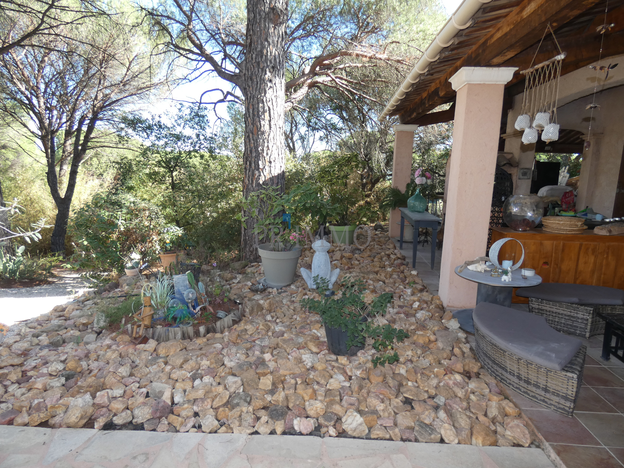 Jardin d'une villa avec des pierres, des plantes et une statue, entouré de pins.