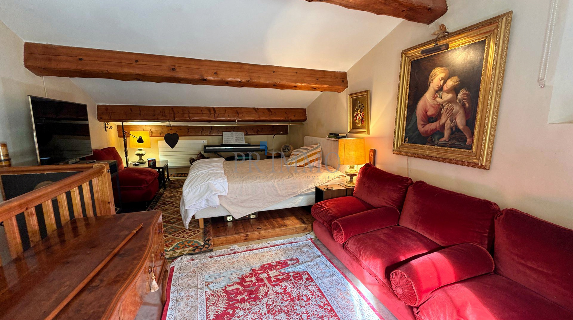 Intérieur d'une villa rénovée avec un salon confortable, un lit et des poutres apparentes.