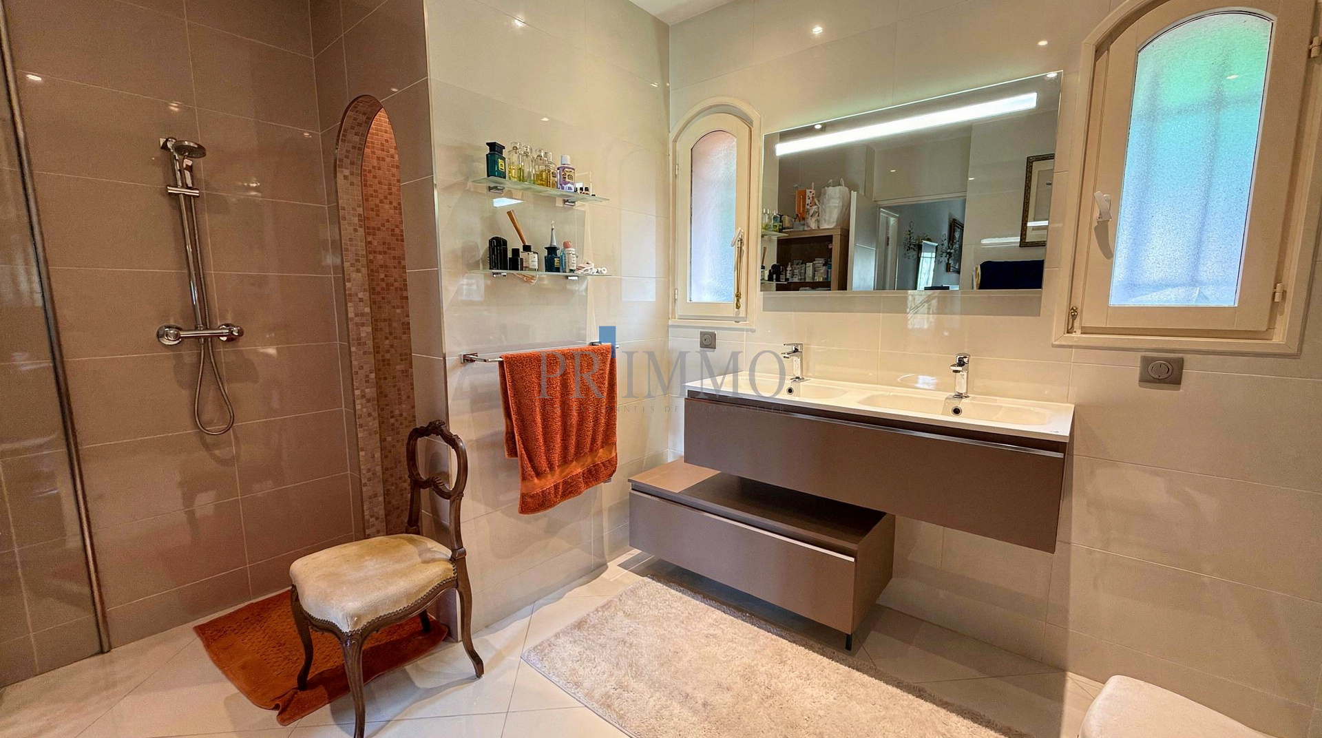 Salle de bain moderne avec douche, lavabo et miroir, décorée de carrelage clair.