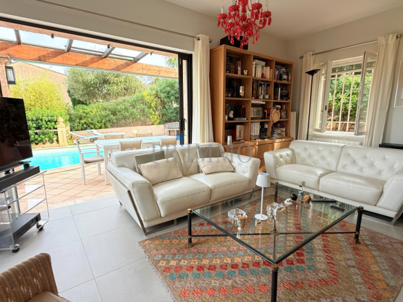 Intérieur d'une villa rénovée avec salon lumineux, vue sur la piscine et jardin.