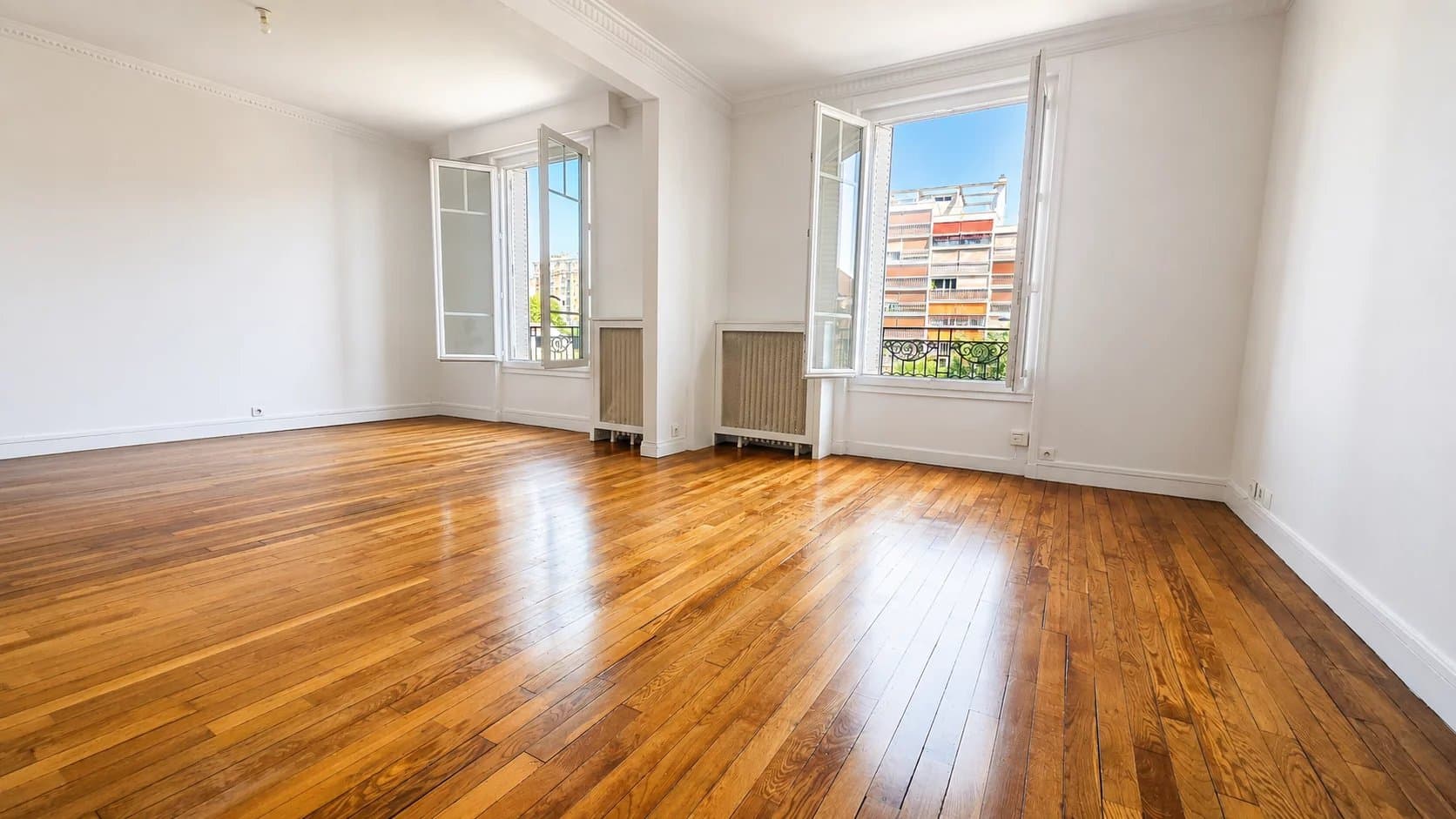 Interior of a spacious apartment with wooden parquet flooring, open windows letting in light.