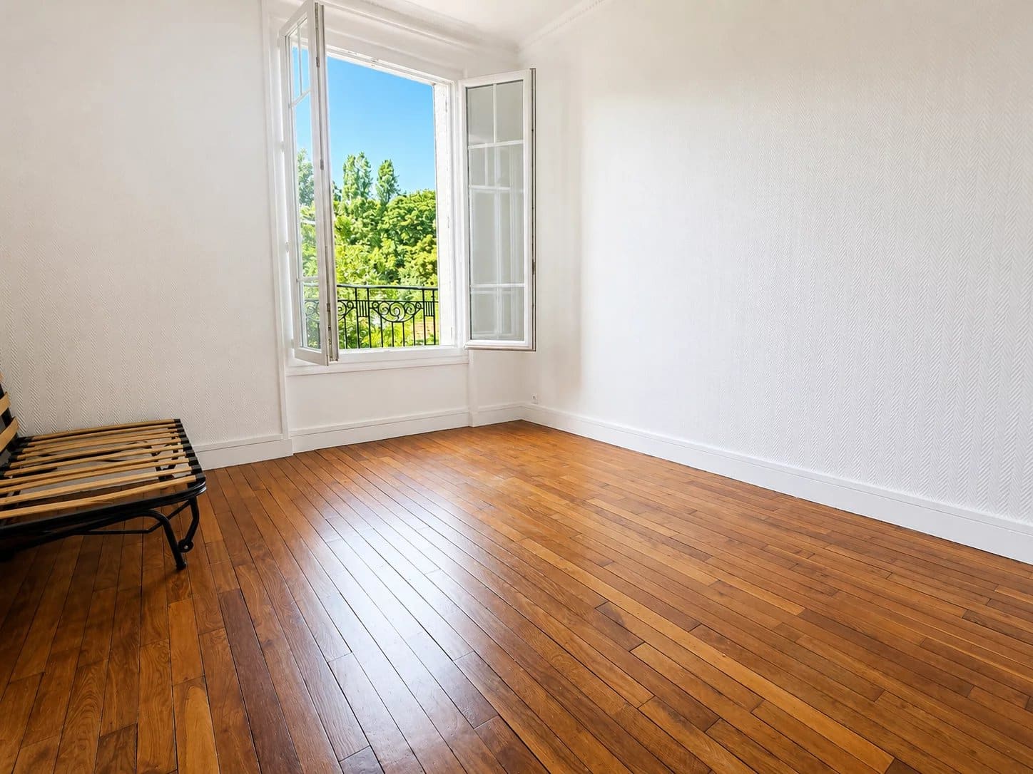 Interior of a renovated apartment with wooden parquet flooring and a window open to the outside.