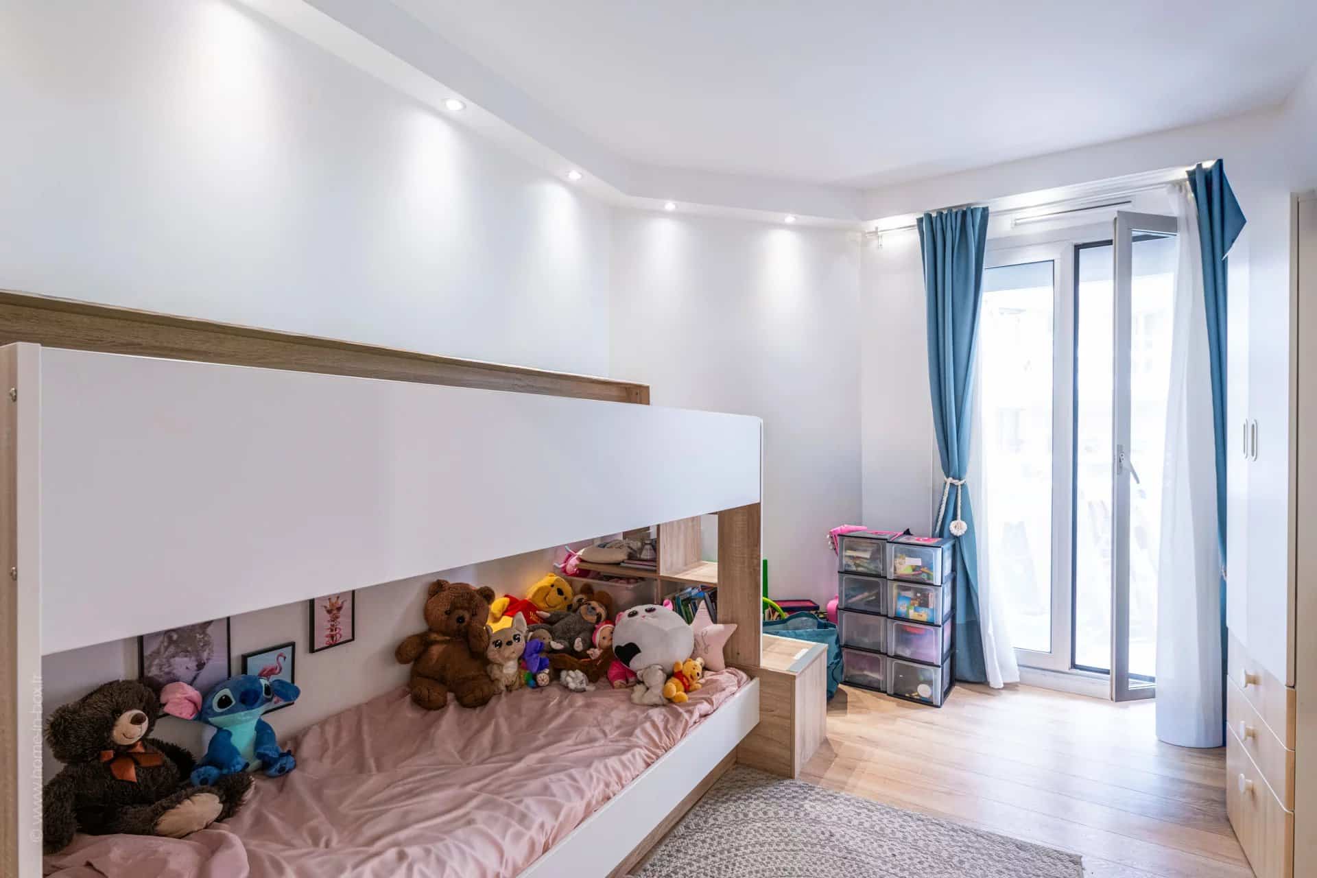 Chambre d'appartement avec lit superposé et jouets, accès à un balcon.