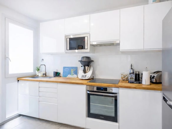 Cuisine moderne d'un appartement à Neuilly-sur-Seine avec meubles blancs et plan de travail en bois.