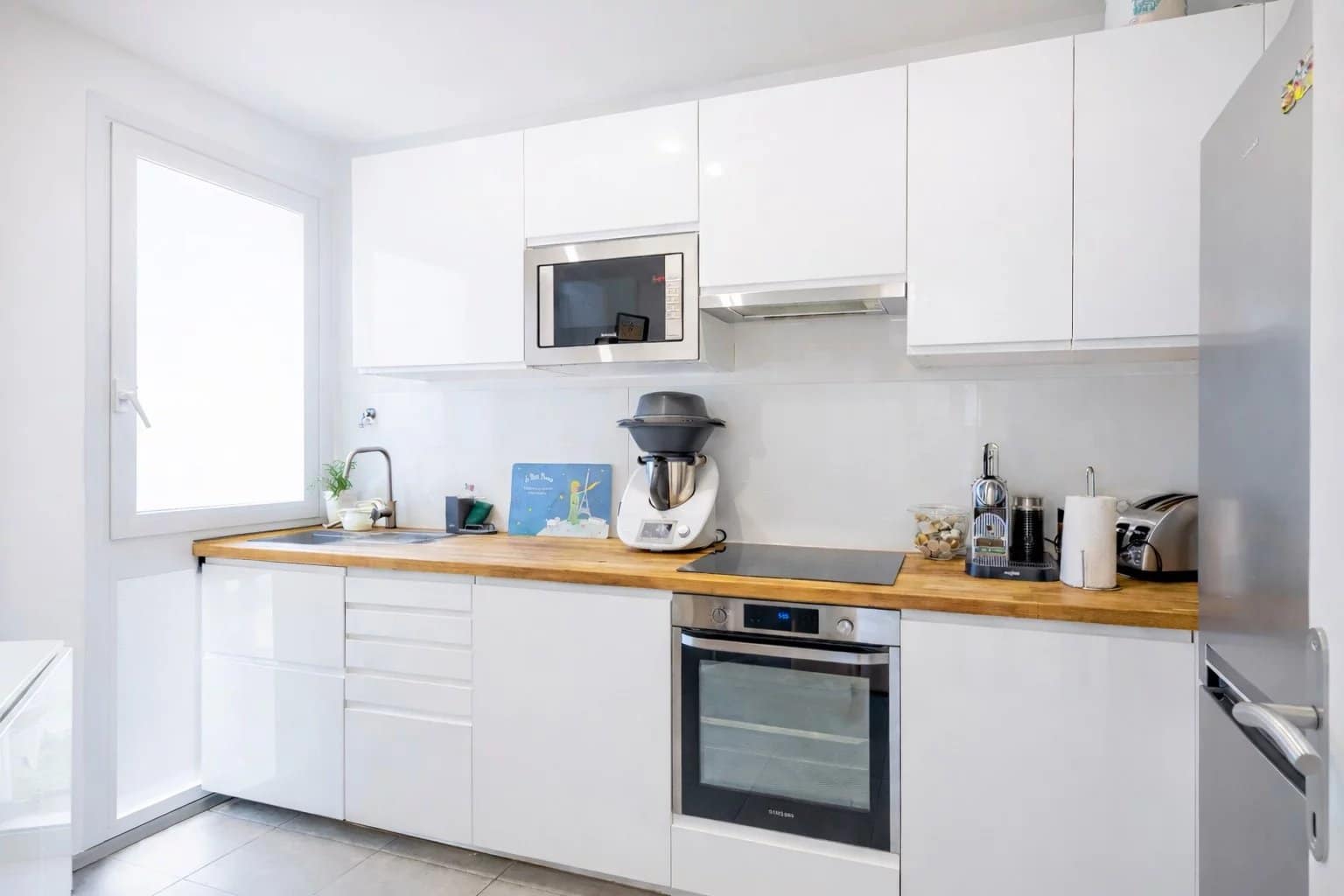 Cuisine moderne d'un appartement à Neuilly-sur-Seine avec meubles blancs et plan de travail en bois.