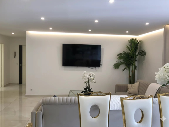 Intérieur d'un appartement moderne avec salon lumineux, télévision murale et décoration élégante.