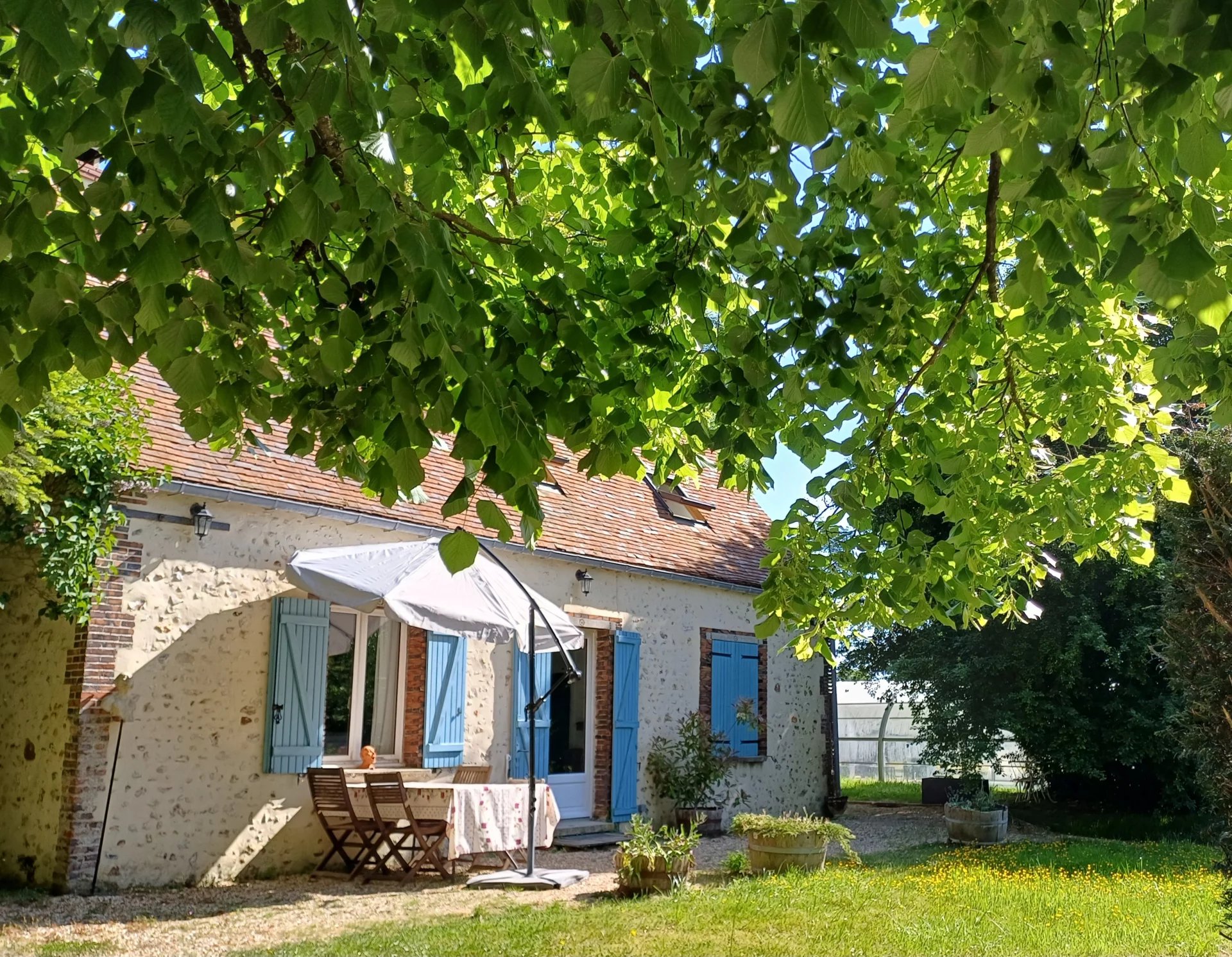 Maison en pierre avec terrasse et parasol, entourée de verdure, dans un parc naturel.